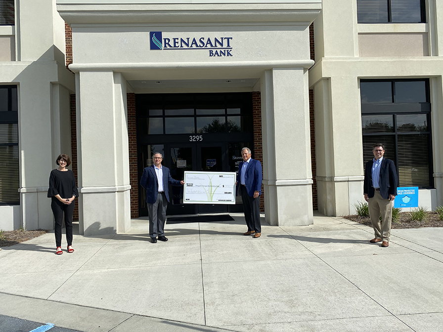 4 people standing in front of Renasant Bank. The two in the middle are holding a giant check