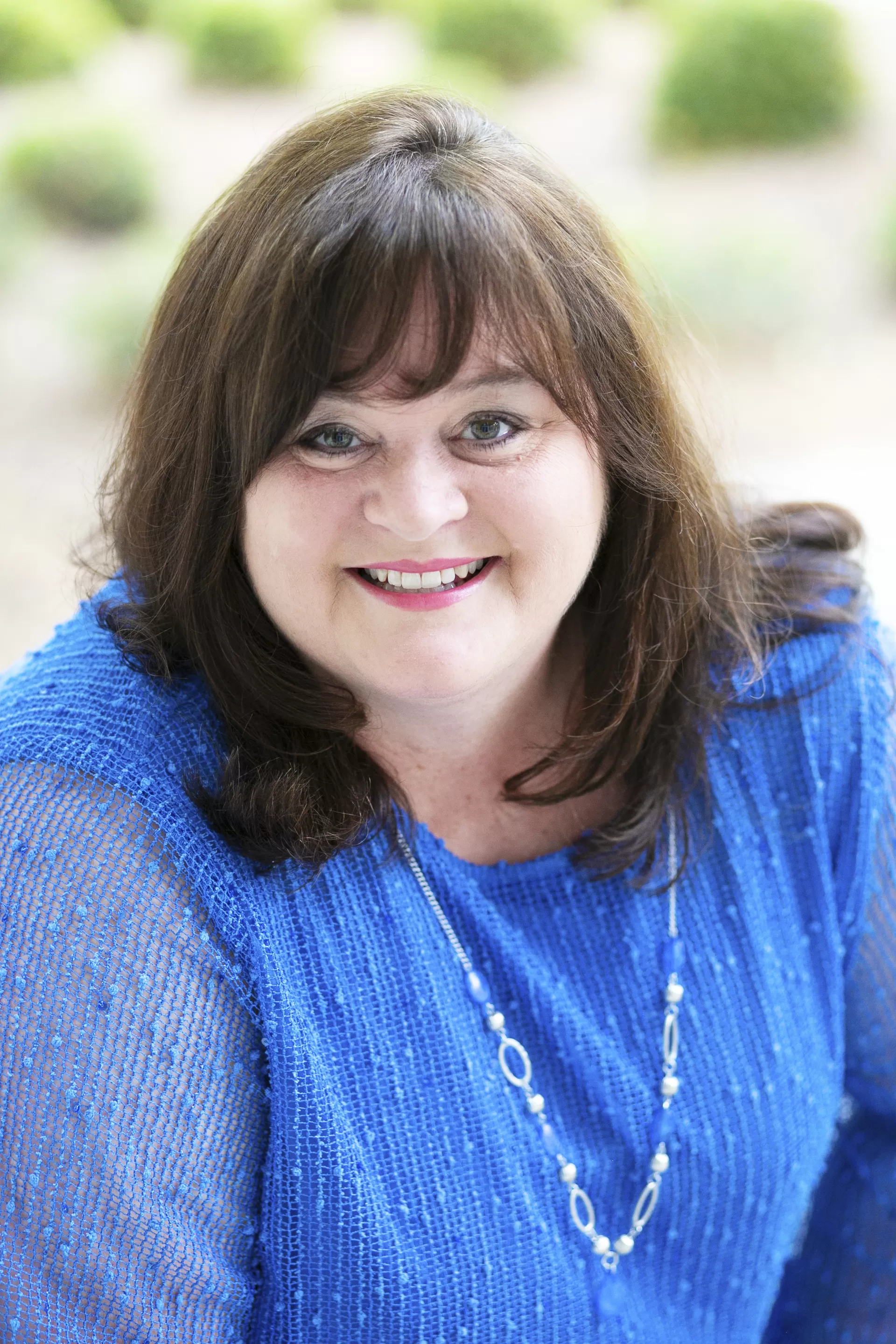 DeAnnia Clements, Wiregrass President, sits facing the viewer, smiling. President Clements has dark brunette hair that adorns her shoulders, and a periwinkle blue knit top on.