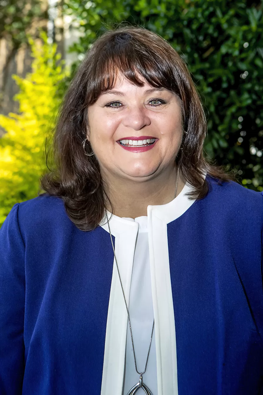 DeAnnia Clements, Wiregrass President, sits facing the viewer, smiling. President Clements has dark brunette hair that adorns her shoulders, and a periwinkle blue knit top on.
