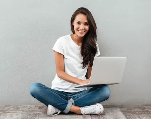 Smiling young lady sitting on the floor with laptop