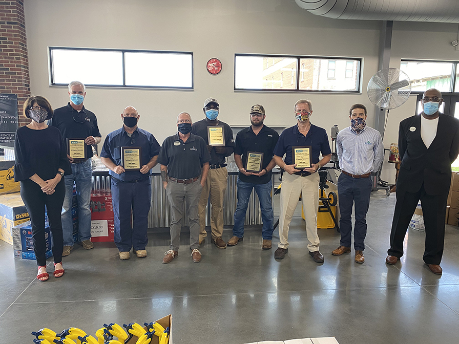 A group of 9 people pose for a photo. Some are holding plaques. Everyone is wearing a facemask.