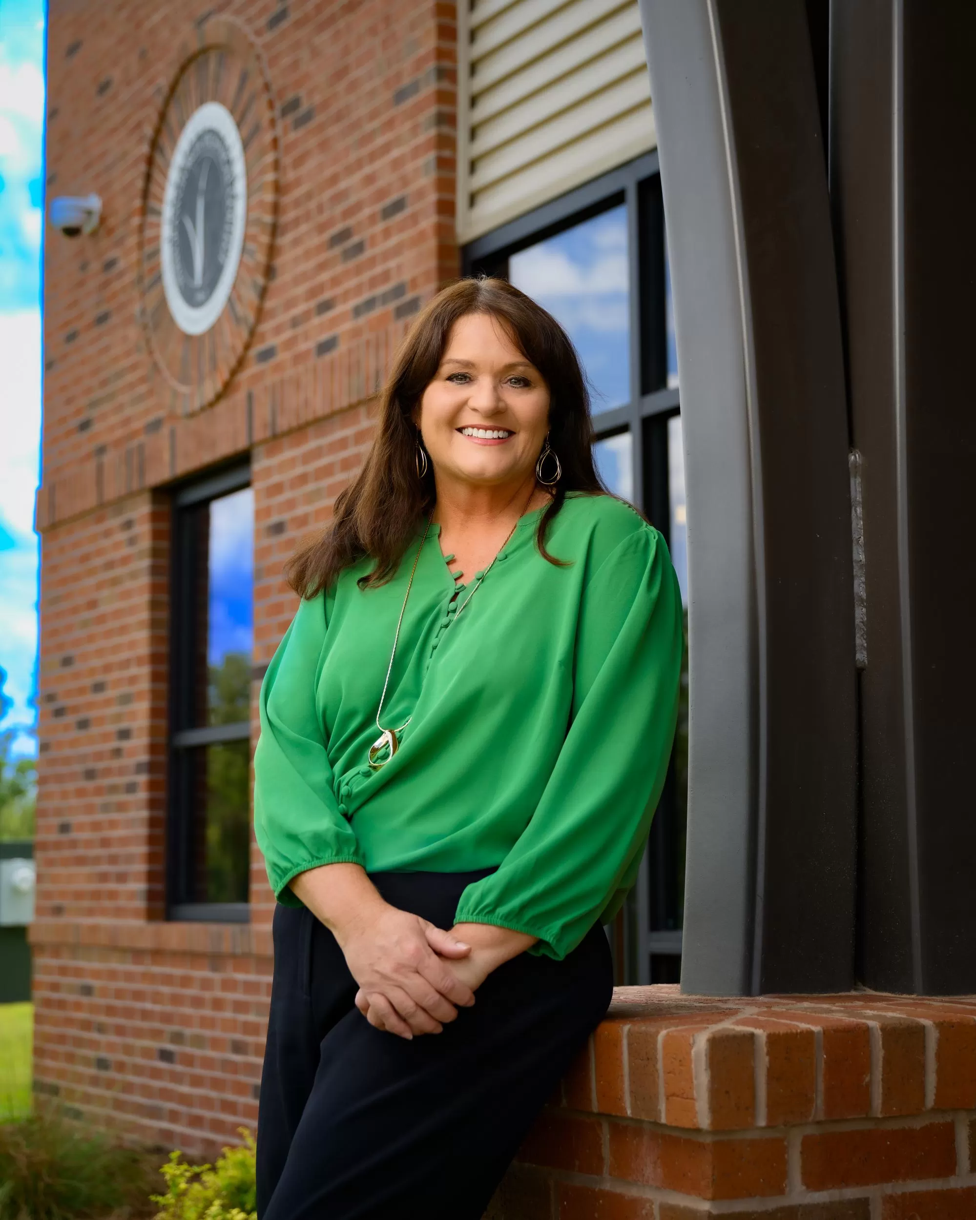 DeAnnia Clements, Wiregrass President, sits facing the viewer, smiling. President Clements has dark brunette hair that adorns her shoulders, and a periwinkle blue knit top on.
